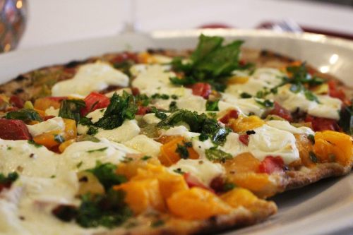 A close-up of a pizza topped with colorful vegetables, herbs, and dollops of cheese on a thin crust.