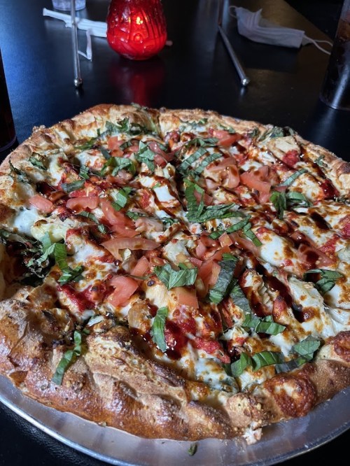 A freshly baked pizza topped with cheese, tomatoes, basil, and drizzled with sauce, served on a silver platter.
