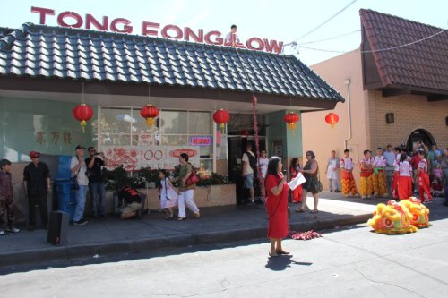 A street scene with a restaurant, red lanterns, and performers in colorful costumes during a celebration.