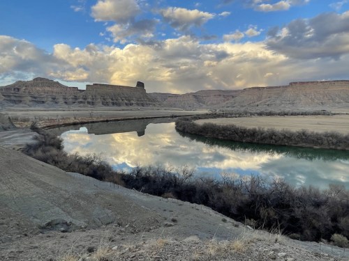 A serene landscape featuring a winding river reflecting clouds and cliffs under a blue sky.