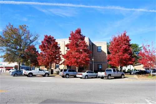 A brick building surrounded by vibrant red trees and parked cars under a clear blue sky.