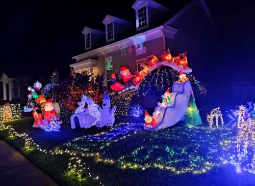 A festive yard display with colorful Christmas lights, inflatable characters, and a decorated house at night.