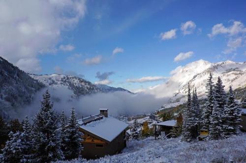 Snow-covered mountains and trees under a blue sky with clouds, overlooking a serene valley and cozy cabins.