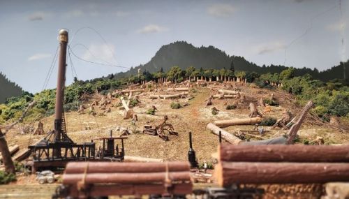 A detailed model of a logging scene with cut trees, a steam-powered machine, and a mountainous backdrop.
