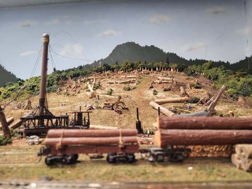 A miniature landscape featuring a logging scene with cut trees, a train, and a mountainous backdrop.