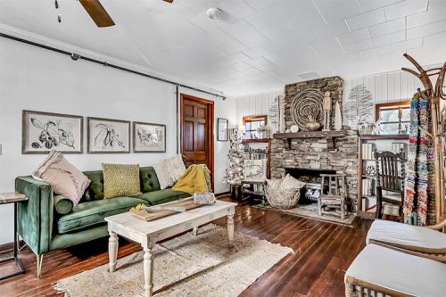 Cozy living room with a green sofa, stone fireplace, wooden furniture, and decorative art on the walls.