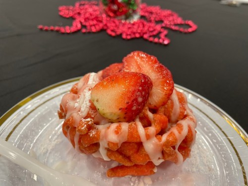 A plate with a colorful dessert topped with strawberries and drizzled with icing, set on a black tablecloth.