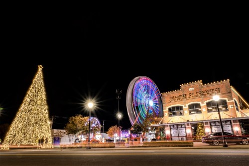 A brightly lit Christmas tree and a colorful Ferris wheel at night, with a historic building in the foreground.