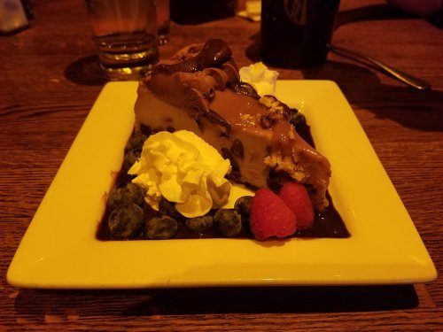 A slice of dessert topped with chocolate, whipped cream, raspberries, and blueberries on a white plate.