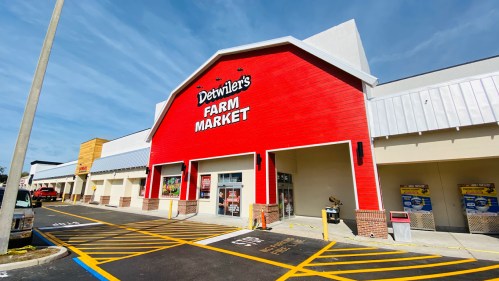 A red barn-style building with "Detwiler's Farm Market" sign, featuring a clear blue sky and parking lot in front.