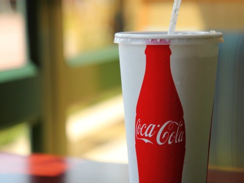 A close-up of a Coca-Cola cup with a straw, set against a blurred background.