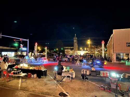 A festive night scene with holiday lights, people gathering, and decorated stalls in a lively street setting.