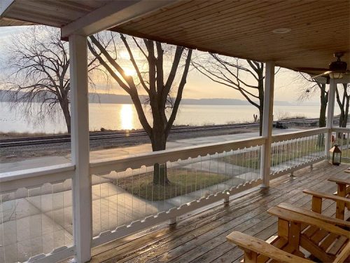 A serene view from a porch overlooking a river at sunset, with trees and a wooden deck in the foreground.