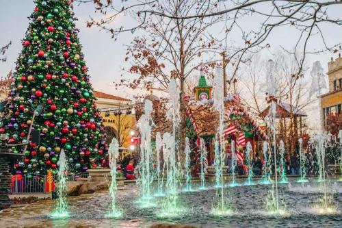 A festive scene featuring a decorated Christmas tree, colorful fountains, and holiday decorations in a lively outdoor setting.
