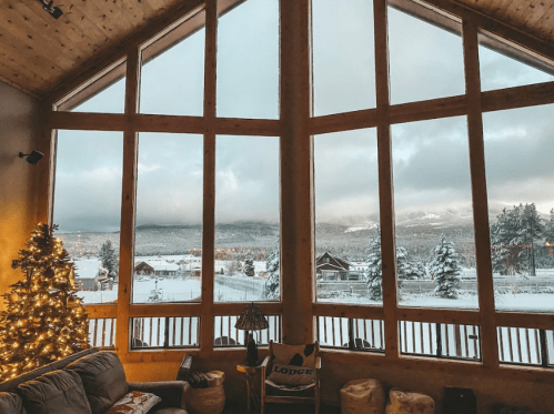 Cozy living room with a Christmas tree, large windows showcasing a snowy landscape and mountains in the background.