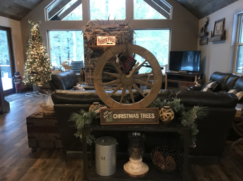 Cozy living room decorated for Christmas, featuring a wagon wheel, tree, and festive decor by a large window.