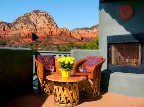 A cozy outdoor seating area with two chairs and a table, overlooking red rock mountains under a clear blue sky.