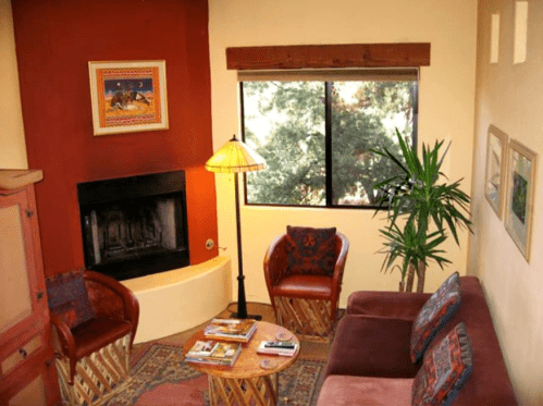 Cozy living room with a fireplace, two chairs, a sofa, and a window overlooking greenery. Warm colors and decor.