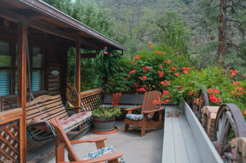 A cozy wooden porch with swings, surrounded by vibrant flowers and greenery, set against a mountainous backdrop.