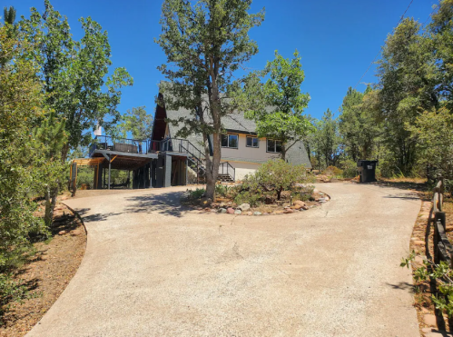 A scenic view of a house surrounded by trees, with a winding driveway leading up to it under a clear blue sky.