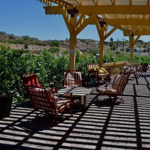 A sunny outdoor patio with colorful chairs and tables, surrounded by greenery and a scenic view.