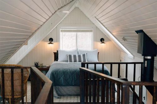 Cozy attic bedroom with a sloped ceiling, large window, and a bed adorned with blue bedding and decorative pillows.