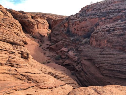 A rugged canyon with red rock formations and sandy ground, under a clear sky.