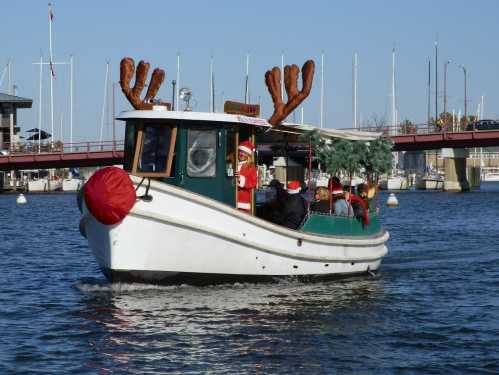 A festive boat decorated with reindeer antlers and a Santa figure, cruising on a calm waterway.