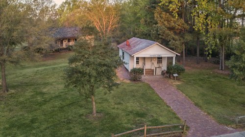 A small, white house with a red roof surrounded by trees and a grassy area, with a path leading to the entrance.