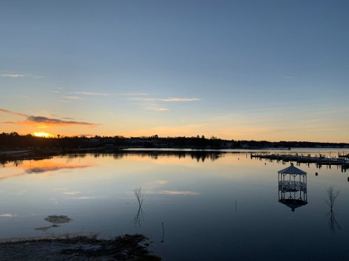 A serene lake at sunset, reflecting colorful skies and a gazebo on the water's edge.