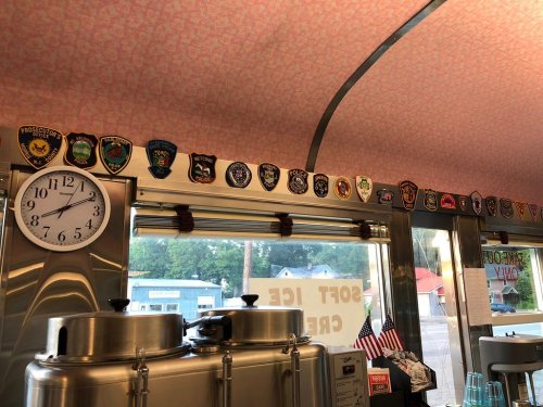 Interior of a diner featuring a clock and a row of various police patches displayed on the wall above metal containers.