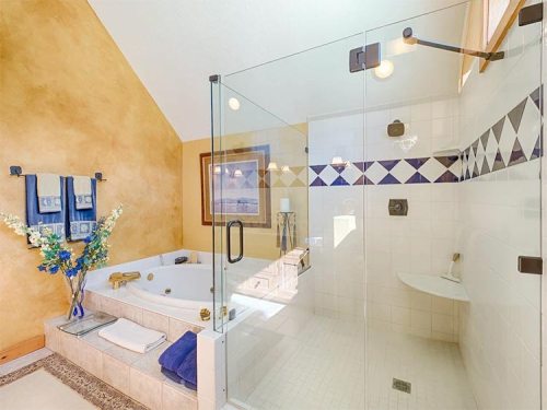 A modern bathroom featuring a glass shower, a large bathtub, and decorative tiles in warm tones.