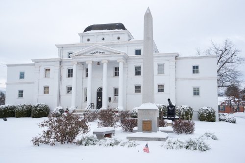 A white building with columns and an obelisk in front, surrounded by snow and winter scenery.