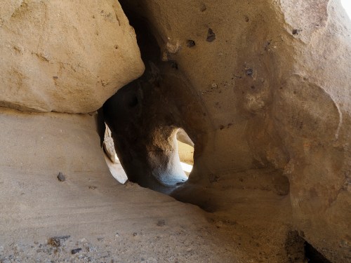 A natural rock formation with a hollowed-out passageway, showcasing textured sandy walls and sunlight filtering through.