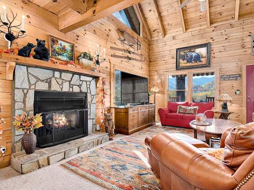 Cozy cabin interior with a stone fireplace, wooden walls, and rustic decor, featuring a red couch and scenic artwork.