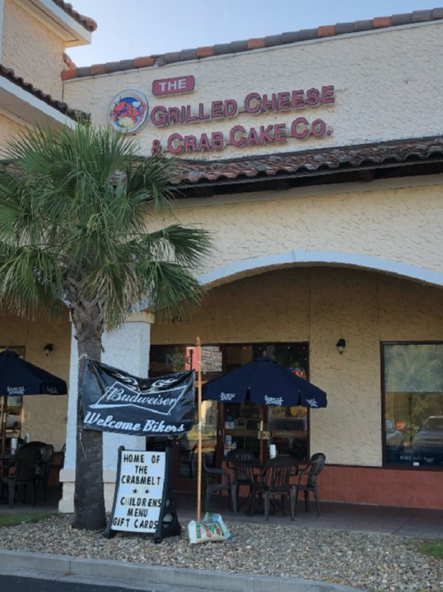 Exterior of a restaurant featuring a sign welcoming bikers, with outdoor seating and umbrellas.