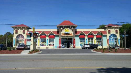 A colorful storefront with a red roof and large windows, featuring a sign that reads "Fun Store" and parked cars outside.