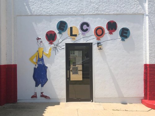 A colorful mural of a clown holding balloons with the word "WELCOME" above a door on a white wall.