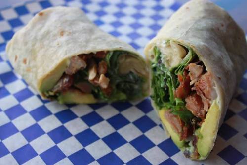 A cut burrito filled with lettuce, chicken, and other ingredients, resting on a blue checkered surface.