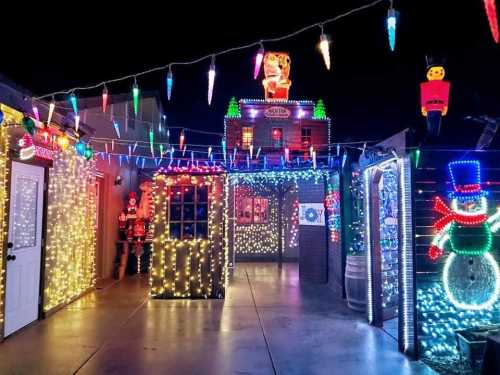 A festive outdoor scene decorated with colorful holiday lights, including snowmen, icicles, and cheerful figures.