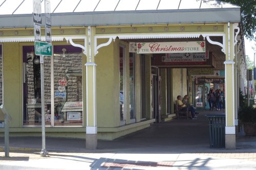A colorful storefront labeled "The Christmas Store" with people walking by on a sunny day.