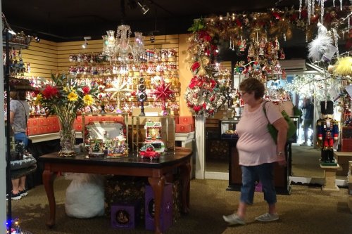 A woman walks through a festive shop filled with colorful decorations and holiday ornaments.