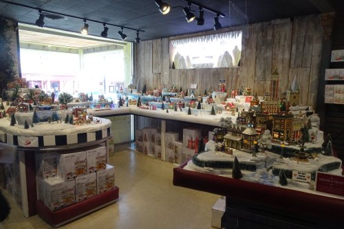 A festive display of miniature holiday villages and decorations in a cozy shop, with snow-covered landscapes.