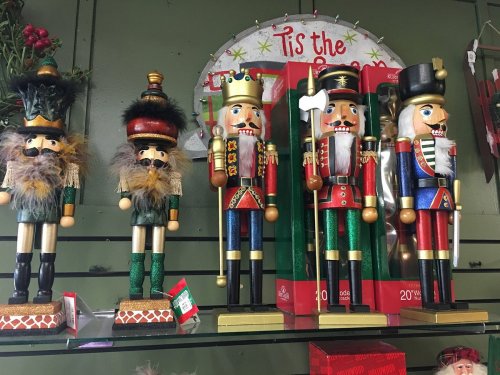 A display of colorful nutcracker figurines in festive attire on a shelf, with holiday decorations in the background.