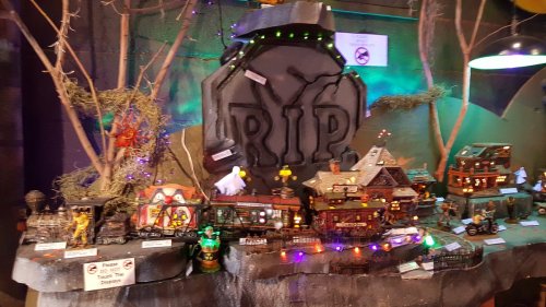 A spooky display of miniature haunted houses and decorations, featuring a large "RIP" tombstone and colorful lights.