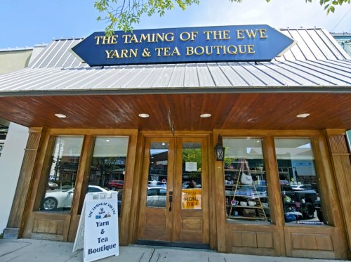 Exterior of "The Taming of the Ewe" yarn and tea boutique, featuring a wooden entrance and a sign above the door.