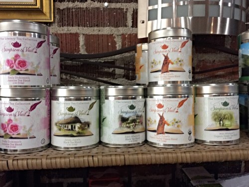 A display of decorative tea tins in various designs, arranged on a shelf against a brick wall.