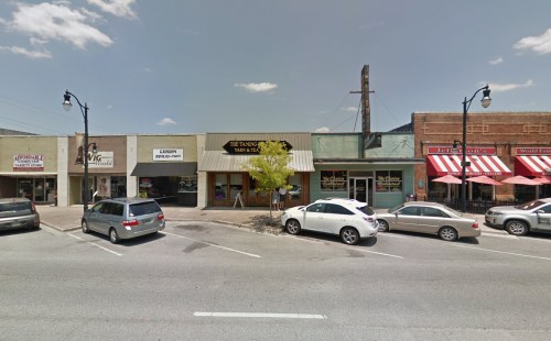 A street view of a small town with shops, restaurants, and parked cars under a clear blue sky.