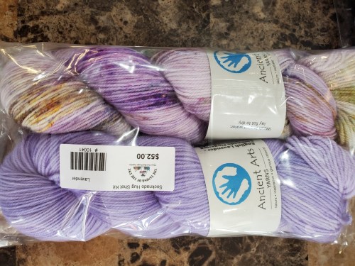 Two skeins of purple yarn in a clear plastic bag, labeled "Ancient Art" with a colorful skein on top.