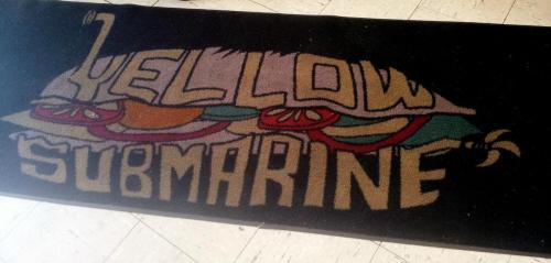 A colorful rug featuring the words "Yellow Submarine" with a whimsical design, including fruits and a submarine illustration.